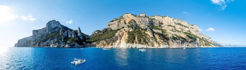 Motor boat off picturesque rocky coast, cliffs with L'Aguglia pinnacle, blue sea and Cala Goloritzé