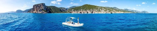 Motor boat off picturesque rocky coast, cliffs and Cala Luna beach, aerial view, Golfo di Orosei,