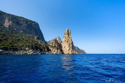 Picturesque rocky coast, cliffs with Pedra Longa pinnacle in the evening light, blue sea, Golfo di