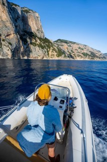 Young woman riding a motorboat along the picturesque rocky coast, cliffs and blue sea, Golfo di