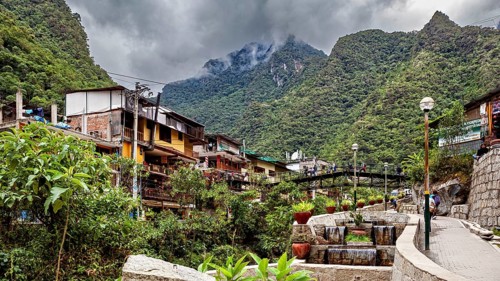 Small village surrounded by mountains under cloudy skies with lush vegetation, The city in the