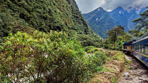 A train travels through a green, mountainous landscape with clouds in the sky, the train through