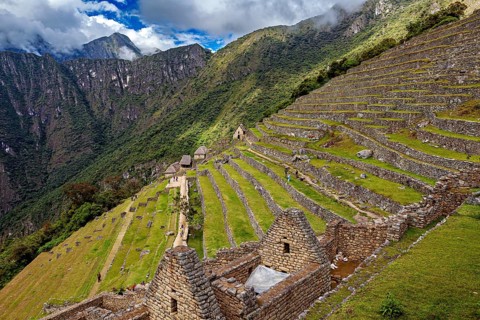Ancient stone structures and terraces on a green mountainside under clouds, the ruins of the Inca