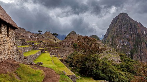 Ruins of Machu Picchu in the foreground against dramatic skies with thick clouds and green areas,