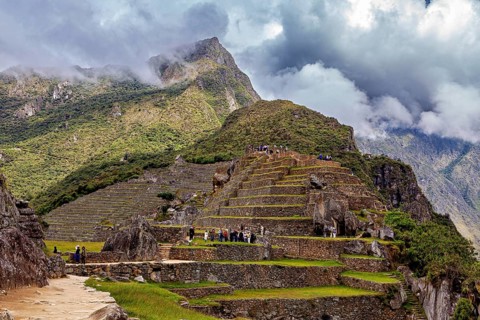 Terraces and ruins on a mountain with dramatic clouds and wandering visitors, The ruins of the Inca