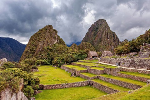 Green terraces and ruins against a dramatic, cloud-covered background, the ruins of the Inca city