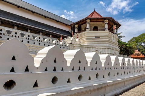 A temple with a white wall and a red roof under a clear sky, The Temple of the Tooth in Kandy Sri