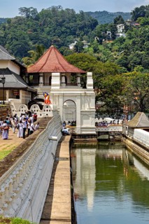 A temple with a pavilion near a river, with people and green surroundings, The Temple of the Tooth