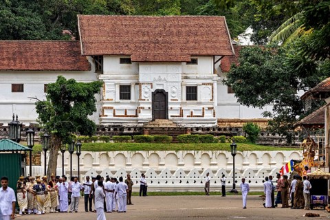A temple with red roof and white walls surrounded by people and trees, The Temple of the Tooth in