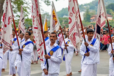 Participants wearing festive white uniforms carry red and white flags in a celebratory parade, The