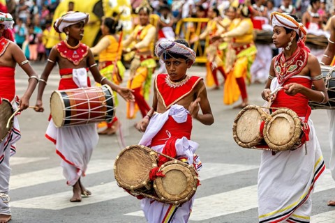 Young drummers in traditional costumes play during a colorful parade on the street, The Perahera