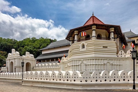Temple complex with white wall, pavilion and colorful flags on a clear day, The Temple of the Tooth