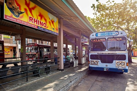 An Ashok Leyland bus at a bus stop with signs and trees in Sri Lanka, bus station in Kandy Sri