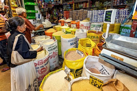 Market customers buy rice from large bags at a well-stocked stand, dealers in the market halls of