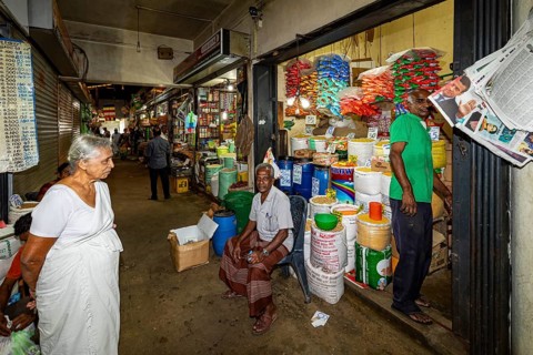 Elderly woman and salesman in a market aisle with colorful goods and packaging, dealer in the