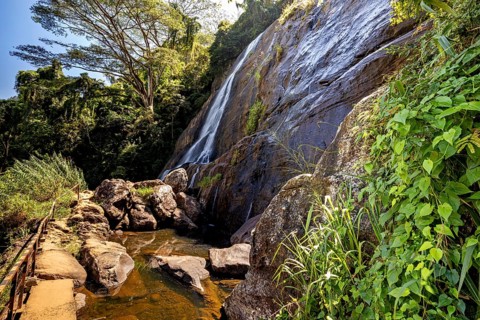 A trail leads past a large waterfall surrounded by lush greenery, waterfall in the highlands near