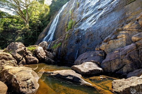 A waterfall flows over large rocks surrounded by trees, waterfall in the highlands near Kandy Sri