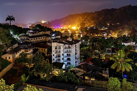 City at night with illuminated buildings and lush vegetation in hilly surroundings, conveys a