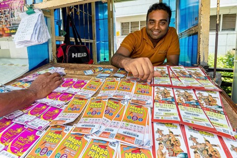 A man smiling behind a sales desk with colorful lottery tickets and tickets, dealer in the market