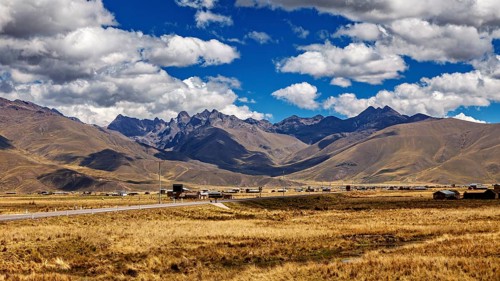 Wide landscape with a road between rolling mountains under a blue sky with clouds, The landscape in