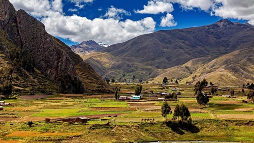 Green fields and hills against a mountain backdrop under a cloudy blue sky, the landscape in the