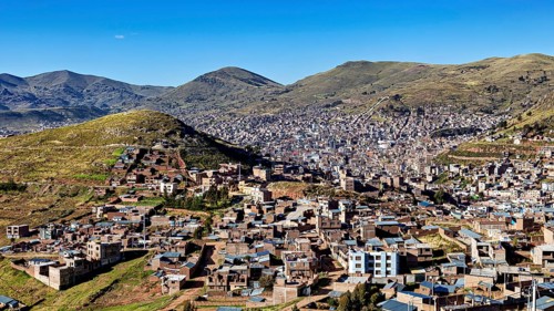 City view of buildings and mountains framed by green hills under a clear blue sky, view of the city