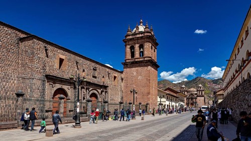 Historic street with impressive bell tower and mountain views, lively with passers-by in clear
