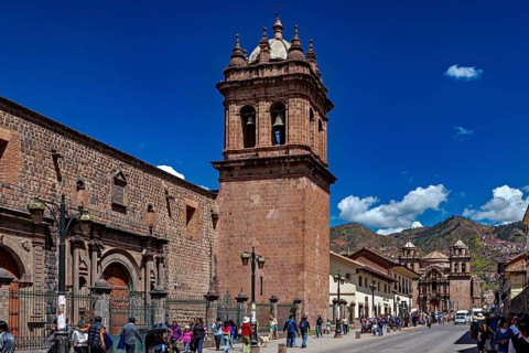 Bell tower on a historic street with people and mountain scenery under clear skies, The churches of