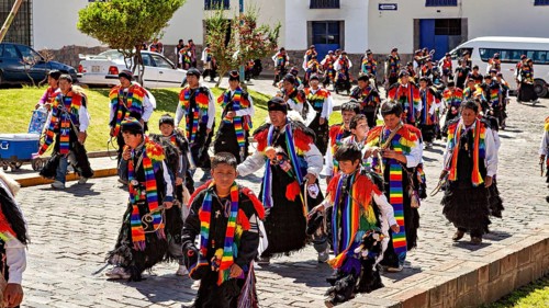 Children and adults in traditional garments move in a colorful procession on the street,
