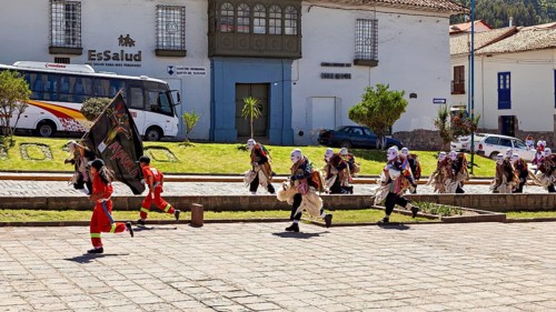 Walking people in masks and costumes cross a paved street, traditional parade of festival groups in