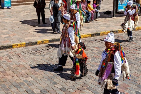 People in traditional costumes, including a child, on a paved street, traditional parade of