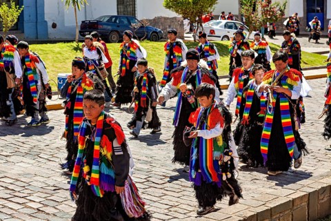 Group of people in colorful costumes walking along the street in sunny weather, traditional parade