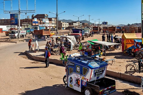 Bustling street scene with tuk-tuk, market stalls and people under bright blue skies, people on the