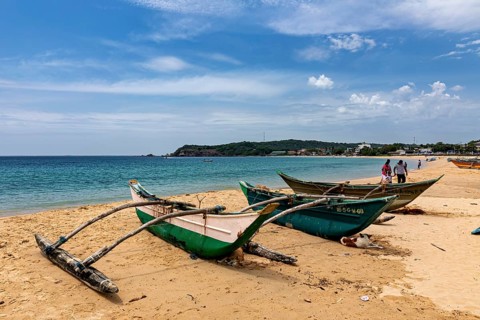 Beach backdrop with green fishing boats in the sand, clear turquoise water and blue sky,