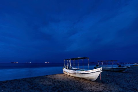 Night landscape with illuminated boat on beach, calm sea and dark sky, traditional boats on