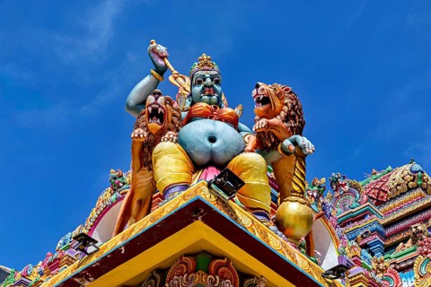 Colourful sculpture of a mythological being with lions on a temple against a blue sky, The Sri