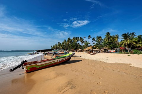 A colorful boat on the beach in front of palm trees and calm sea, clear sky, peaceful, Trincomalee