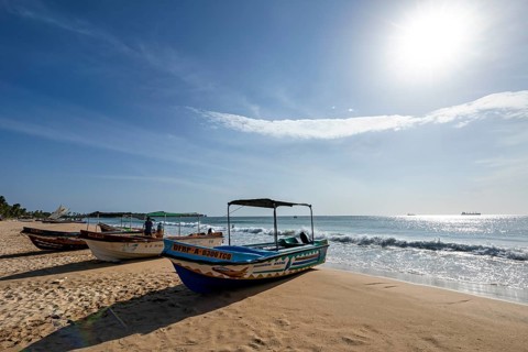 Boats are moored on a sunny beach with soft waves and clear skies, a peaceful atmosphere,