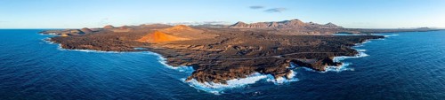 Coast with lava fields, volcanic landscape near Los Hervideros with red volcano Montaña Bermeja, in