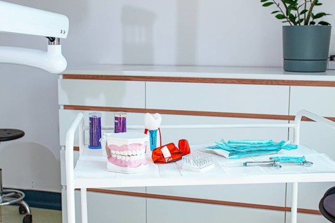 Various instruments, dental models, and hygiene items are laid out on the table in the dental