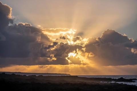 Dramatic cloudy sky with sunbeams at sunset, seaside coast with volcanic rocks, La Santa,