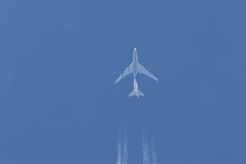 Boeing 747 jumbo jet cargo aircraft flying in a blue sky with contrails or vapour trails behind,
