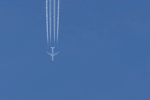 Jet passenger aircraft flying in a blue sky with contrails or vapour trails behind, England, United