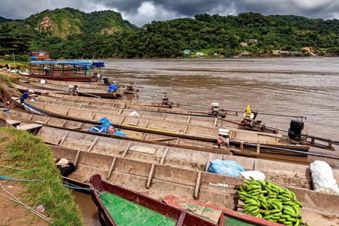Wooden boats with bananas and motors in front of a mountainous landscape, longboat on a river near