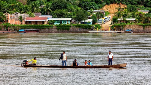 A boat with people passes by a tropical village surrounded by lush nature, people on boats near