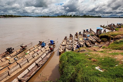 Wooden boats lie on the riverbank under a cloudy sky surrounded by lush greenery, longboat on a