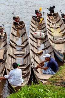 People sit in wooden barges with motors on the banks of a river, longboat on a river near