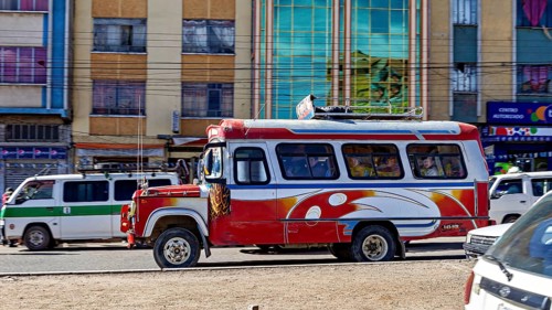 A red and white bus travels through a busy street surrounded by multi-colored buildings, traffic in