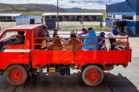 A red truck transports several people through a rural area in a quiet atmosphere, Road traffic in
