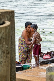 A woman washes a child at the river, both laugh and wear colorful clothes, a woman washes at a lake